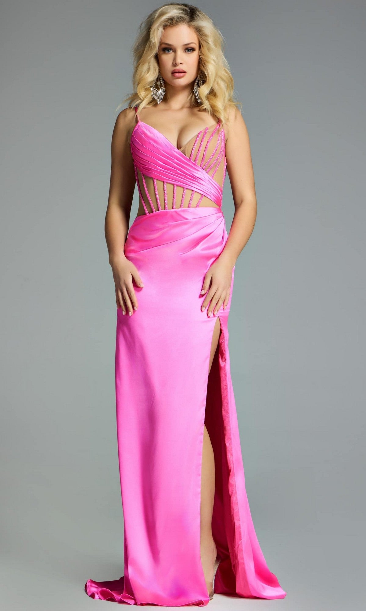 A woman models the Jovani 43681 Long Prom Dress—a bright pink evening gown with an illusion bodice, satin sheath skirt, cutout details, and thigh-high slit—standing against a plain gray background.